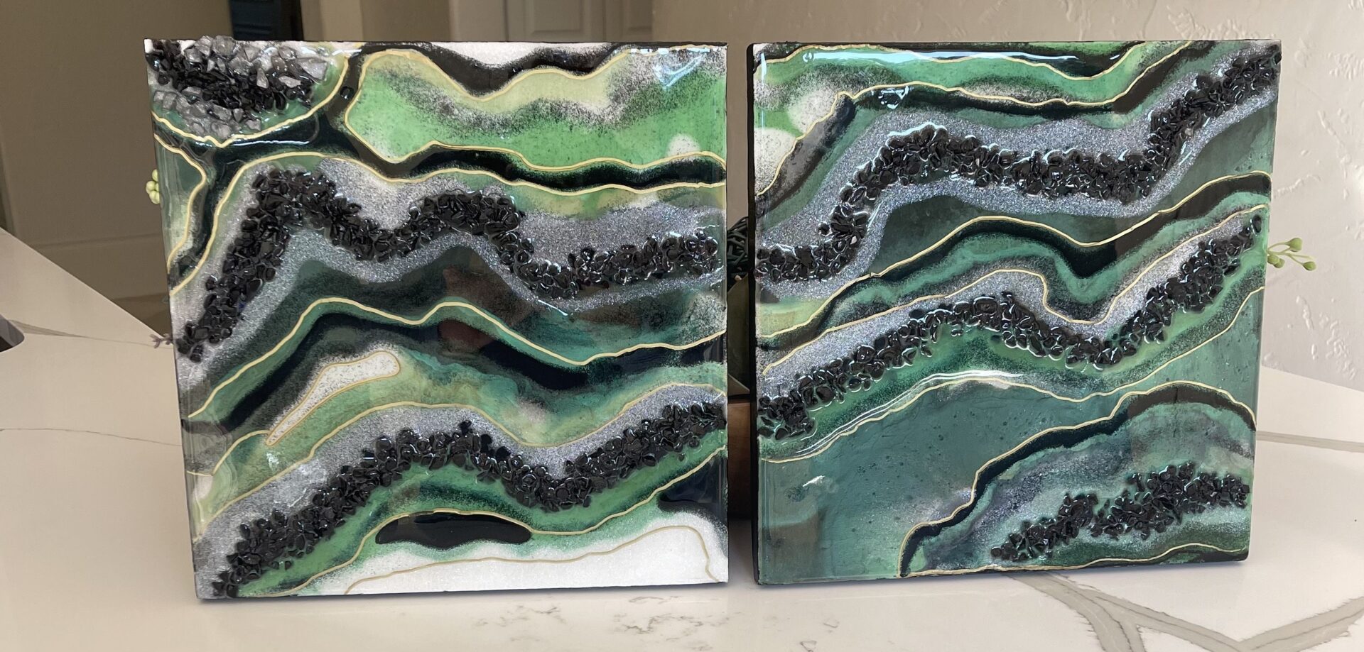 Two paintings of green and white waves on a table.